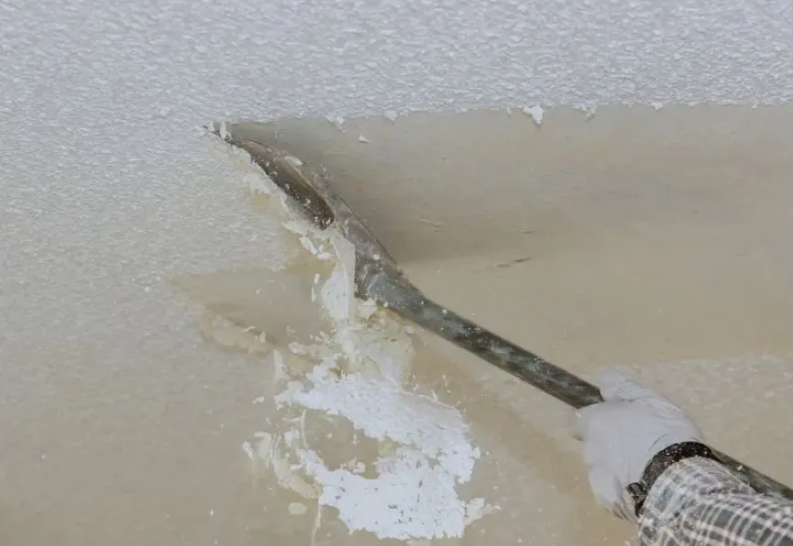 Popcorn ceiling texture being scraped away with a wide blade during a stipple removal